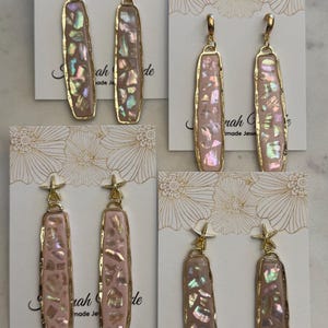 May include: Gold-toned earrings with rectangular, iridescent pink inserts. Some earrings feature a small gold starfish charm. The earrings are displayed on cards with floral designs and the text "Sarah G made Jewels".