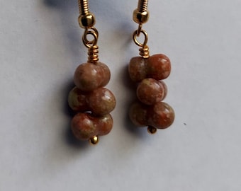 May include: A pair of gold earrings with three brown and white speckled beads on each earring.