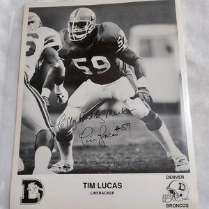 May include: Black and white photograph of a football player in a Denver Broncos uniform, number 59. The image includes the player's signature and the text "Tim Lucas, Linebacker". The Broncos logo is also visible.