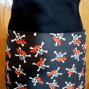 May include: Black apron with a large pocket on the front. The pocket is decorated with a repeating pattern of white skull and crossbones with red bandanas.