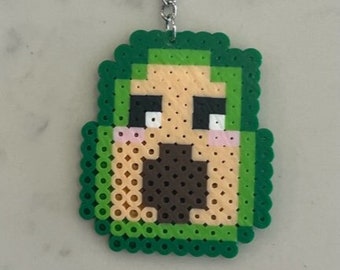 May include: Green and brown pixelated avocado keychain with a silver chain and ring.