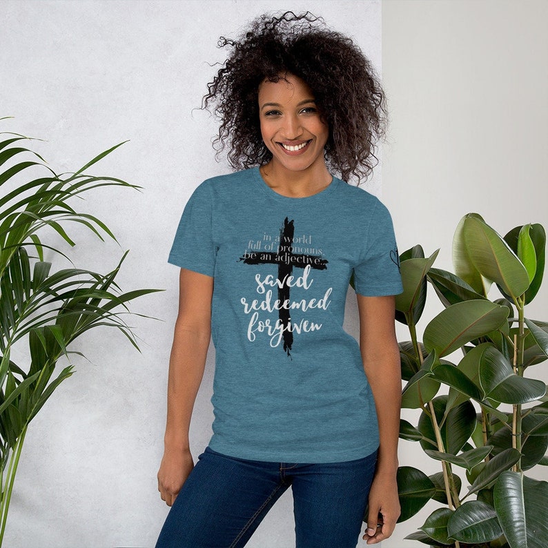 May include: A teal blue t-shirt with a black cross graphic and the text "in a world full of pronouns be an adjective saved redeemed forgiven".