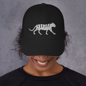 May include: A black baseball cap with a white embroidered image of a tiger walking. The cap has a curved brim and an adjustable strap.