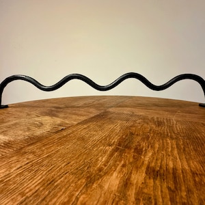 Könnte beinhalten: Ein schwarzer Metallgriff mit wellenförmigem Design, befestigt an einer Holzoberfläche.