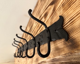 May include: A black metal coat rack with multiple hooks mounted on a wooden wall. The wood has a dark brown, burnt finish.