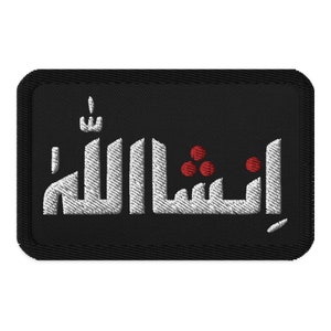 Puede incluir: Parche rectangular negro bordado con escritura árabe blanca y tres puntos rojos. El parche tiene un borde negro y una apariencia texturizada, adecuado para coser o planchar sobre tela.