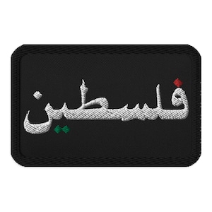 Può includere: Toppa rettangolare nera con ricamo bianco in scrittura araba. La scritta dice "Palestina", con accenti verdi e rossi. La toppa ha un bordo nero.
