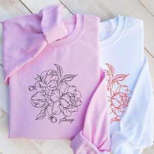 May include: Two pink and white sweatshirts with a floral design. The pink sweatshirt has a black outline of peonies and the text "Peony". The white sweatshirt has a red outline of peonies and the text "Peony".