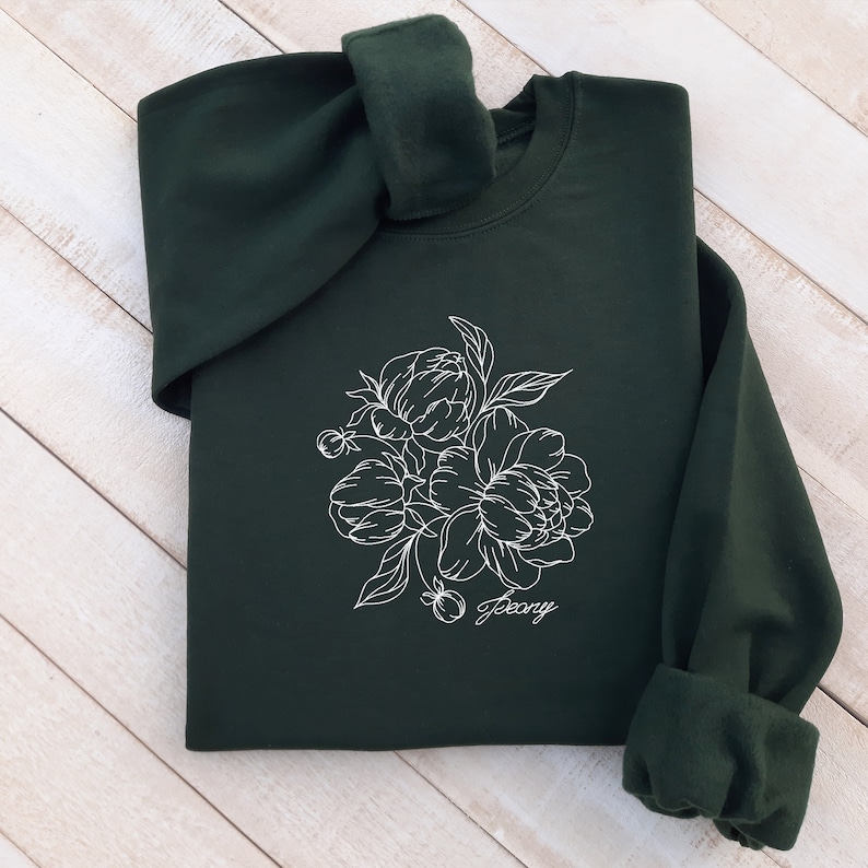 May include: A dark green sweatshirt with a white outline of a bouquet of peonies and the word "peony" written underneath.