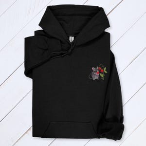 May include: Black hooded sweatshirt with a kangaroo pocket. The sweatshirt features a small embroidered design of a gray mouse holding red berries and green leaves on the left chest. The hoodie has a drawstring and a hood.