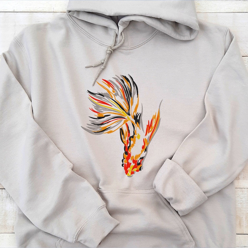 Peut inclure: Un sweat &agrave; capuche gris clair avec un motif brod&eacute; de poisson rouge avec des d&eacute;tails orange, jaune, noir et gris.