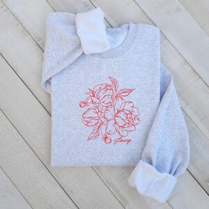 May include: A gray sweatshirt with a red line drawing of a bouquet of peonies and the word "Peony" printed below the flowers.