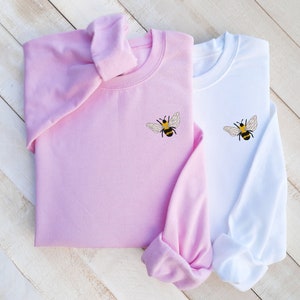 May include: Two sweatshirts, one pink and one white, with embroidered bumblebees on the front.