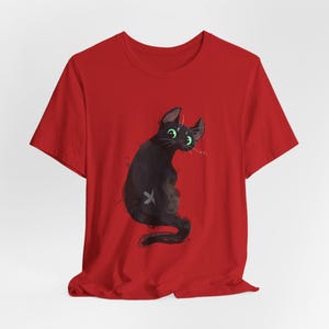 May include: Red t-shirt with a black cat illustration. The cat has green eyes and is looking to the right. The cat is sitting on its hind legs with its tail curled around its body.