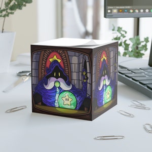 May include: A square notepad with a cartoon illustration of a wizard wearing a blue robe and holding a green orb with a yellow star inside. The wizard is sitting on a throne in a stone room with a red and gold archway.