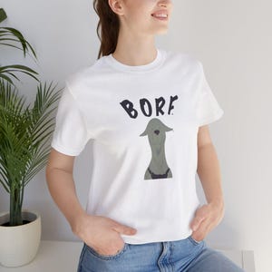 Puede incluir: Camiseta blanca con un gráfico negro de un perro con la palabra "BORF" encima.