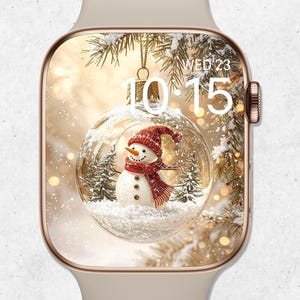 Pode incluir: Um smartwatch bege com moldura dourada exibe uma cena de inverno. A tela mostra um boneco de neve dentro de um globo de neve, usando um cachecol e chapéu vermelhos. A hora é 10:15 da quarta-feira.