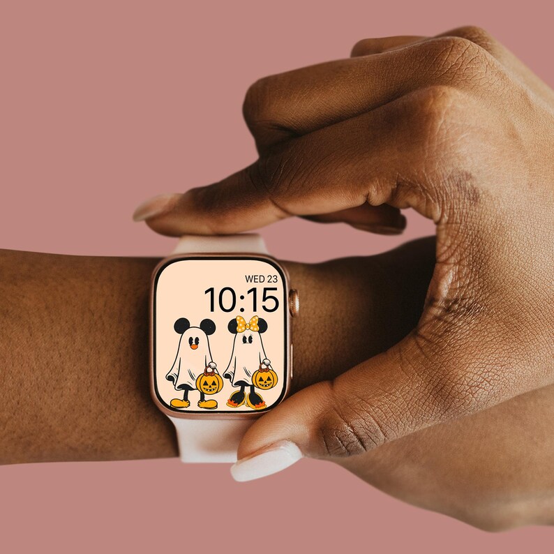 May include: A white smartwatch with a gold band displays a Halloween-themed watch face with Mickey Mouse and Minnie Mouse dressed as ghosts holding jack-o'-lanterns. The watch face also displays the time, 10:15, and the day, WED 23.