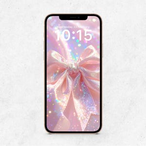 Peut inclure: Un smartphone doré affiche un fond d'écran avec un nœud rose et des paillettes, indiquant l'heure 10h15. La date est mercredi 23 février. Le nœud est l'élément central, avec une esthétique douce et romantique.