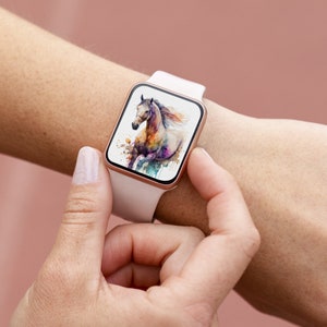 May include: A white smartwatch with a rose gold band displays a colorful watercolor painting of a horse running. The horse is white with splashes of pink, blue, and green.