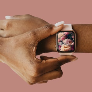 May include: A white smartwatch with a rose gold band and a floral screen saver. The watch is on a person's wrist.