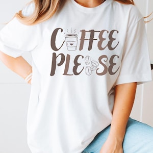 May include: White t-shirt with the text "Coffee Please" in brown lettering. The design includes a coffee cup and coffee beans. The person is wearing light blue jeans and holding a disco ball.