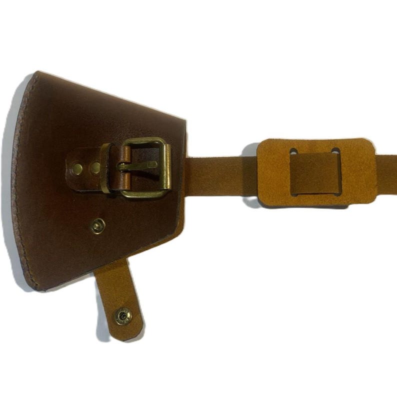 May include: A brown leather axe sheath with a brass buckle and strap. The sheath is designed to hold an axe head and has a riveted construction. The strap is adjustable and made of a lighter brown leather.