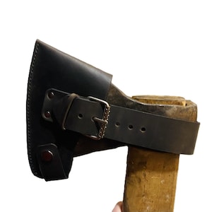 May include: A black leather axe sheath with a buckle closure and a strap, protecting the axe head. The axe handle is made of wood.