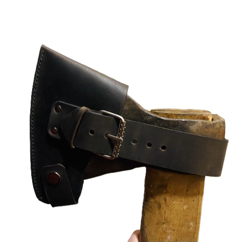 May include: A black leather axe sheath with a buckle closure and a strap, protecting the axe head. The axe handle is made of wood.