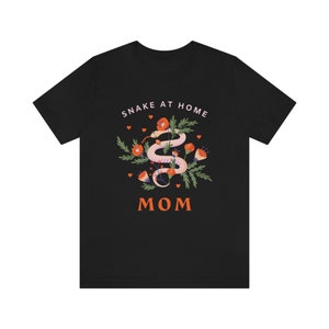 May include: Black t-shirt with a white graphic of a snake in a floral arrangement. The text "Snake at Home Mom" is printed on the shirt.