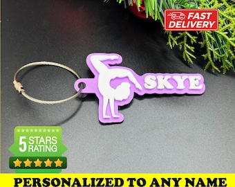 May include: Purple keychain with a gymnast silhouette and the name "Skye" in white lettering. The keychain has a silver metal ring. The text "Personalized to any name" and "Many colors available" is also included in the image.