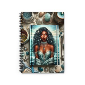 May include: A spiral bound notebook with a teal cover featuring a painting of a woman with long blue hair and a teal dress. The woman is wearing jewelry and is surrounded by seashells, crystals, and other decorative items.