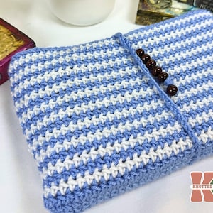 May include: A handmade crochet book cover in blue and white stripes. The cover is secured with a blue crocheted strap and dark brown wooden beads. The item is a handmade book sleeve.