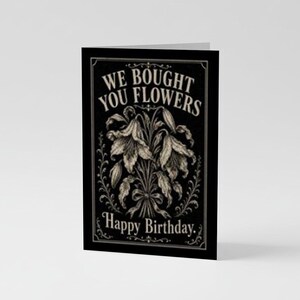 May include: A black greeting card featuring a white illustration of a bouquet of lilies tied with a ribbon. The text at the top reads WE BOUGHT YOU FLOWERS and the text at the bottom reads Happy Birthday. The design is framed by a decorative border.