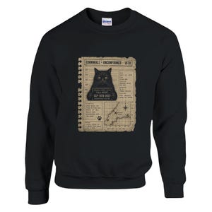 May include: A black crewneck sweatshirt featuring a graphic print of a vintage-style Cornwall Unconfirmed 1978 police field report. The design includes a black cat, a height chart, a map of Bodmin Moor, and text detailing a 1978 sighting.