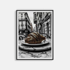 May include: A framed print showing a croissant on a white plate, placed on a marble-effect table. The croissant has a distinctive design, with a pattern of numbers and text. The background is a black and white street scene.