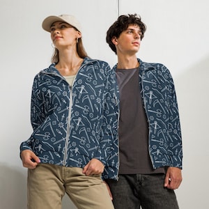 May include: Navy blue zip-up jackets with a white weapon pattern. The jackets feature a variety of weapons, including axes, swords, and scythes. The jackets are worn by two people, one wearing a baseball cap.
