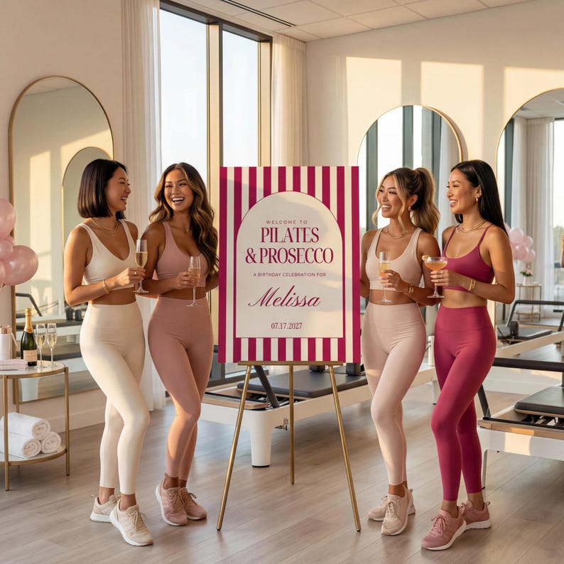 May include: Four women in athletic wear pose with drinks near a sign that reads "Welcome to Pilates & Prosecco" for Melissa's birthday. The sign is white with burgundy stripes and text. The women wear matching leggings and tops in cream, pink, and burgundy.