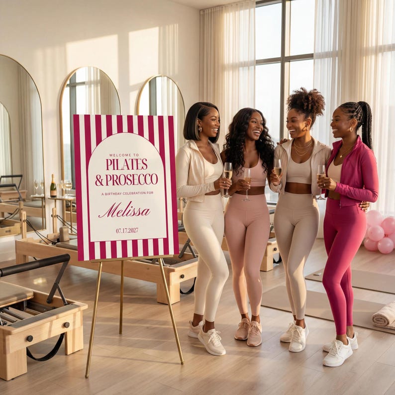 May include: A sign with the text "WELCOME TO PILATES & PROSECCO" and the name "Melissa" is displayed on a gold easel. Four women in athletic wear are holding champagne flutes. The sign has a burgundy and white striped design.