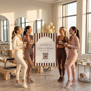 May include: Four women in athletic wear stand near a sign that reads "Melissa's Mats & Martinis Birthday Party." The sign is on a gold easel. The women are holding drinks and smiling. The room has large windows and exercise equipment.