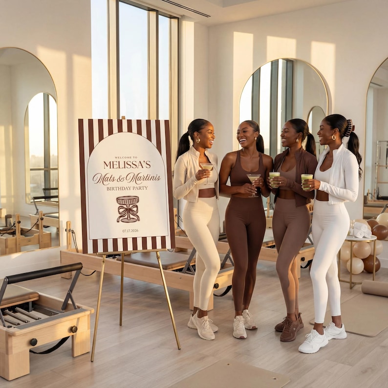 May include: Four women in athletic wear, holding drinks, stand near a sign that reads "Melissa's Mats & Martinis Birthday Party." The sign is brown and white, and the women are wearing shades of brown and white athletic outfits.