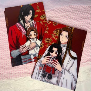 Può includere: Due stampe artistiche rosse e dorate con illustrazioni in stile anime. Ogni stampa raffigura un personaggio che tiene in mano una bambola. Lo sfondo è rosso intenso con motivi floreali dorati. Le bambole indossano abiti bianchi e rossi.
