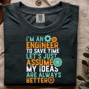 May include: A dark charcoal gray t-shirt featuring the text "I'M AN ENGINEER TO SAVE TIME LET'S JUST ASSUME MY IDEAS ARE ALWAYS BETTER" in a distressed font. The design includes orange and light blue gear icons interspersed with the lettering.