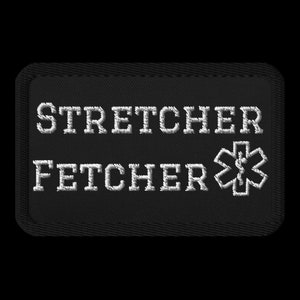 May include: Black rectangular patch with white embroidered text reading "STRETCHER FETCHER" and a medical star emblem. The patch has a black border, likely for medical professionals.