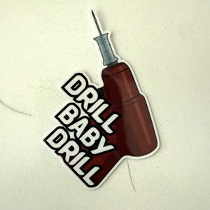 Könnte beinhalten: Ein Aufkleber mit einer Cartoon-Bohrmaschine in Braun- und Grautönen mit den Worten "DRILL BABY DRILL" in fetten weißen Buchstaben mit schwarzer Umrandung. Der Aufkleber befindet sich auf einer weißen Oberfläche.