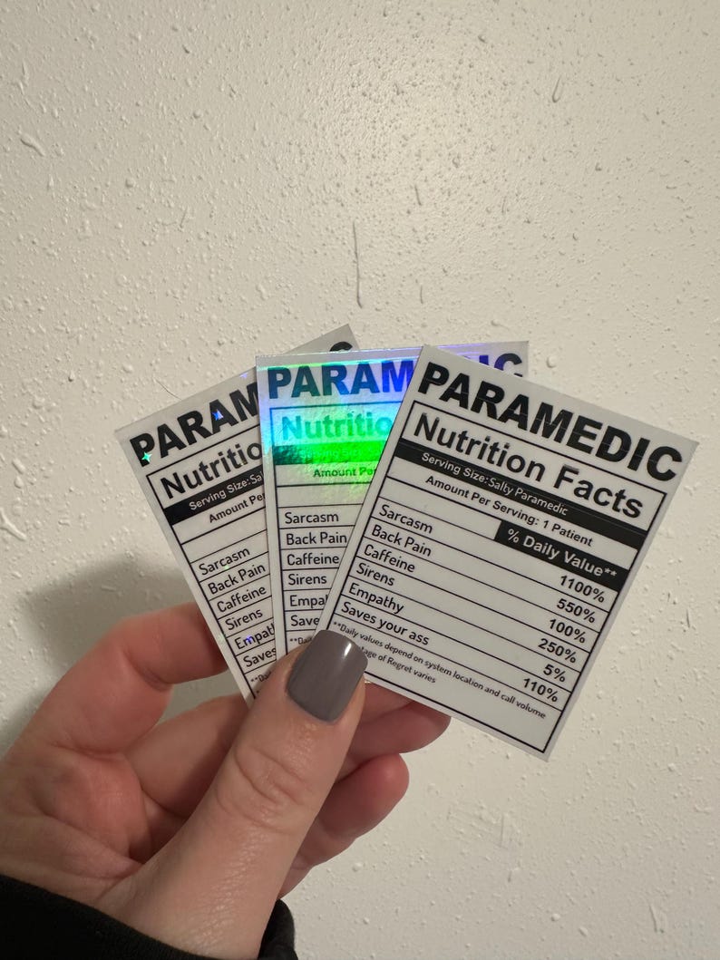 Puede incluir: Tres pegatinas con fondo blanco y texto negro que dice "PARAMEDIC Nutrition Facts". Las pegatinas enumeran datos humor&iacute;sticos de "% Daily Value" como "Sarcasm" y "Caffeine". Las pegatinas se sostienen en una mano.