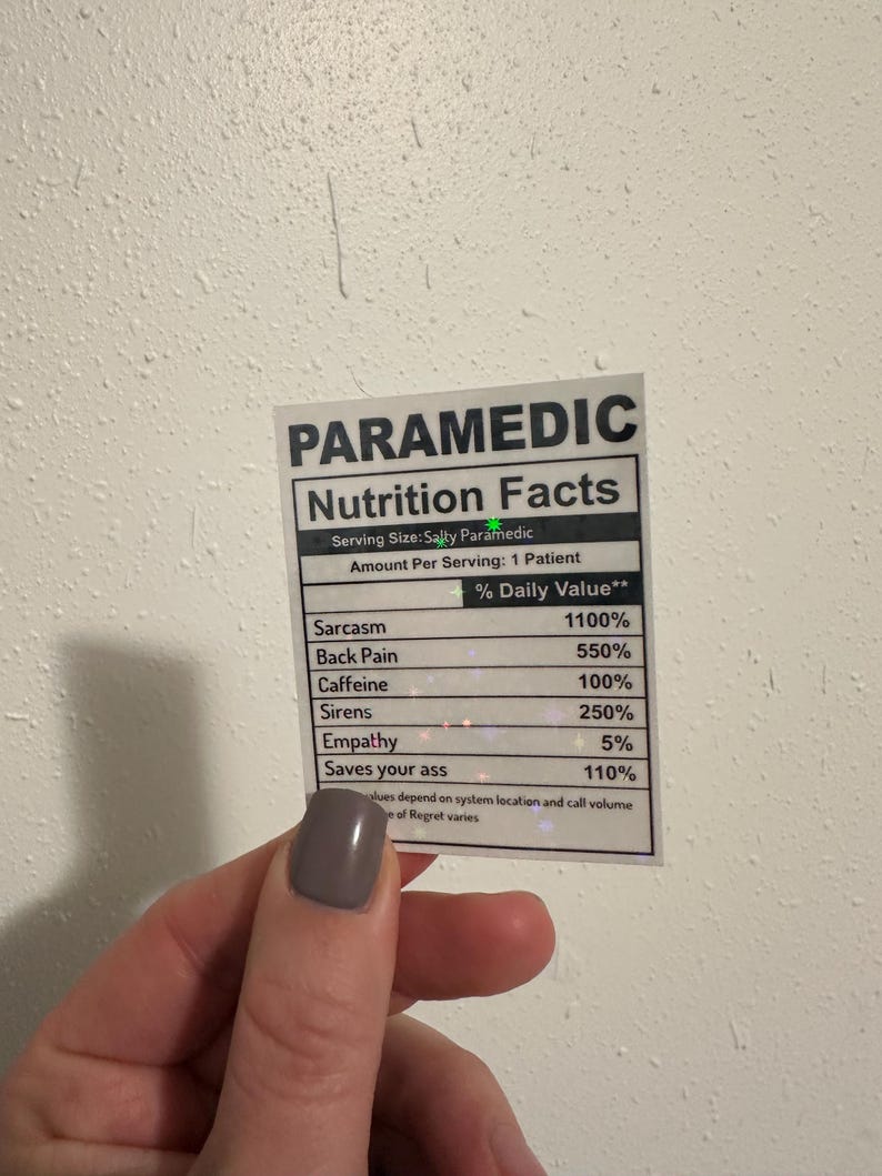 Puede incluir: Una pegatina con el texto "PARAMEDIC Nutrition Facts" enumera los valores diarios para el trabajo de un param&eacute;dico, incluyendo sarcasmo, dolor de espalda, cafe&iacute;na, sirenas, empat&iacute;a y "Saves your ass".