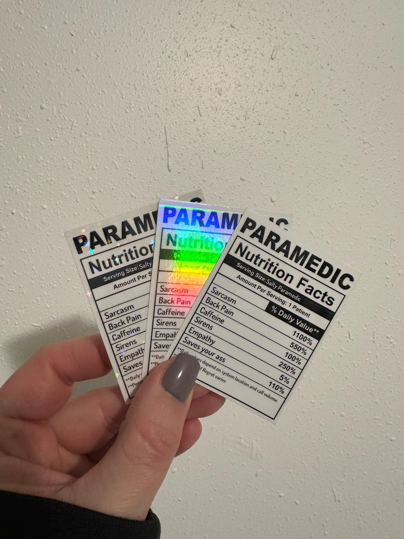Puede incluir: Tres pegatinas con tem&aacute;tica de param&eacute;dico, dise&ntilde;adas como etiquetas de informaci&oacute;n nutricional. Las pegatinas presentan "ingredientes" humor&iacute;sticos como sarcasmo y cafe&iacute;na. El texto "PARAMEDIC Nutrition Facts" est&aacute; en la parte superior.