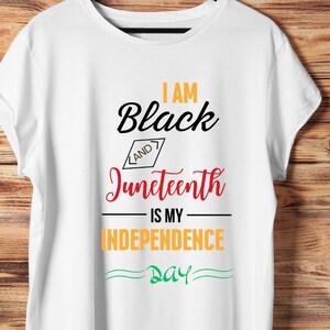May include: White t-shirt with the text "I am Black and Juneteenth is my Independence Day" in black, red, and yellow lettering.