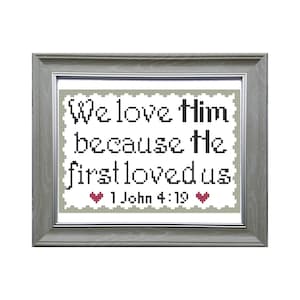May include: A framed cross-stitch with the text "We love Him because He first loved us" and the scripture reference "1 John 4:19" with two red hearts.